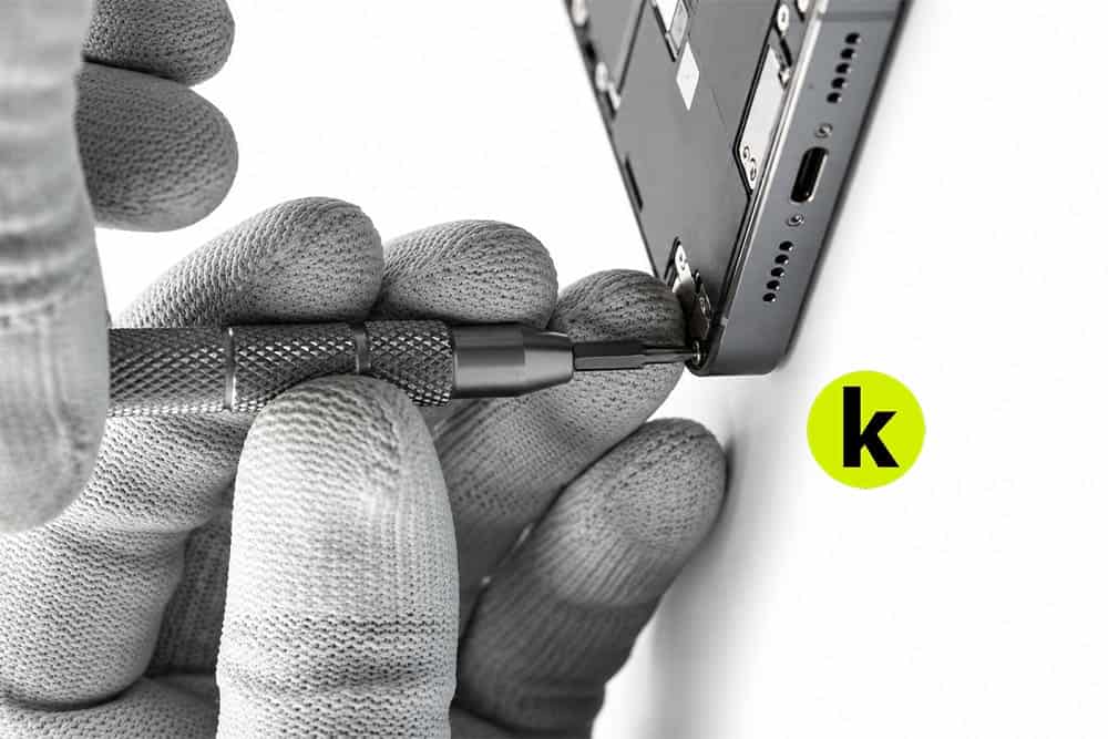 Мастер откручивает крепеж возле разъема зарядки iPhone 18 Pro Max перед разборкой корпуса